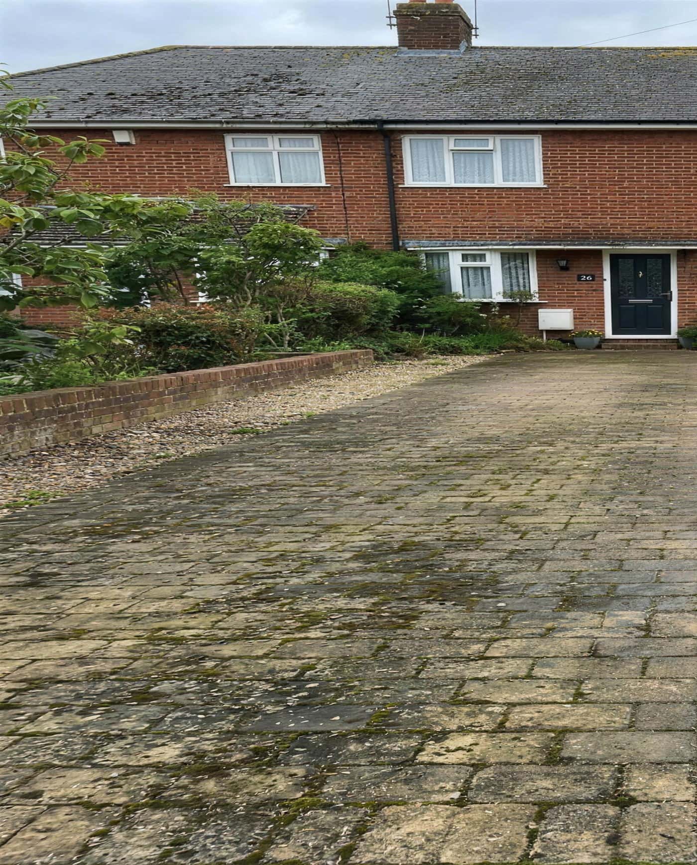 A block-paved driveway covered in green algae and dirt, with the house behind it